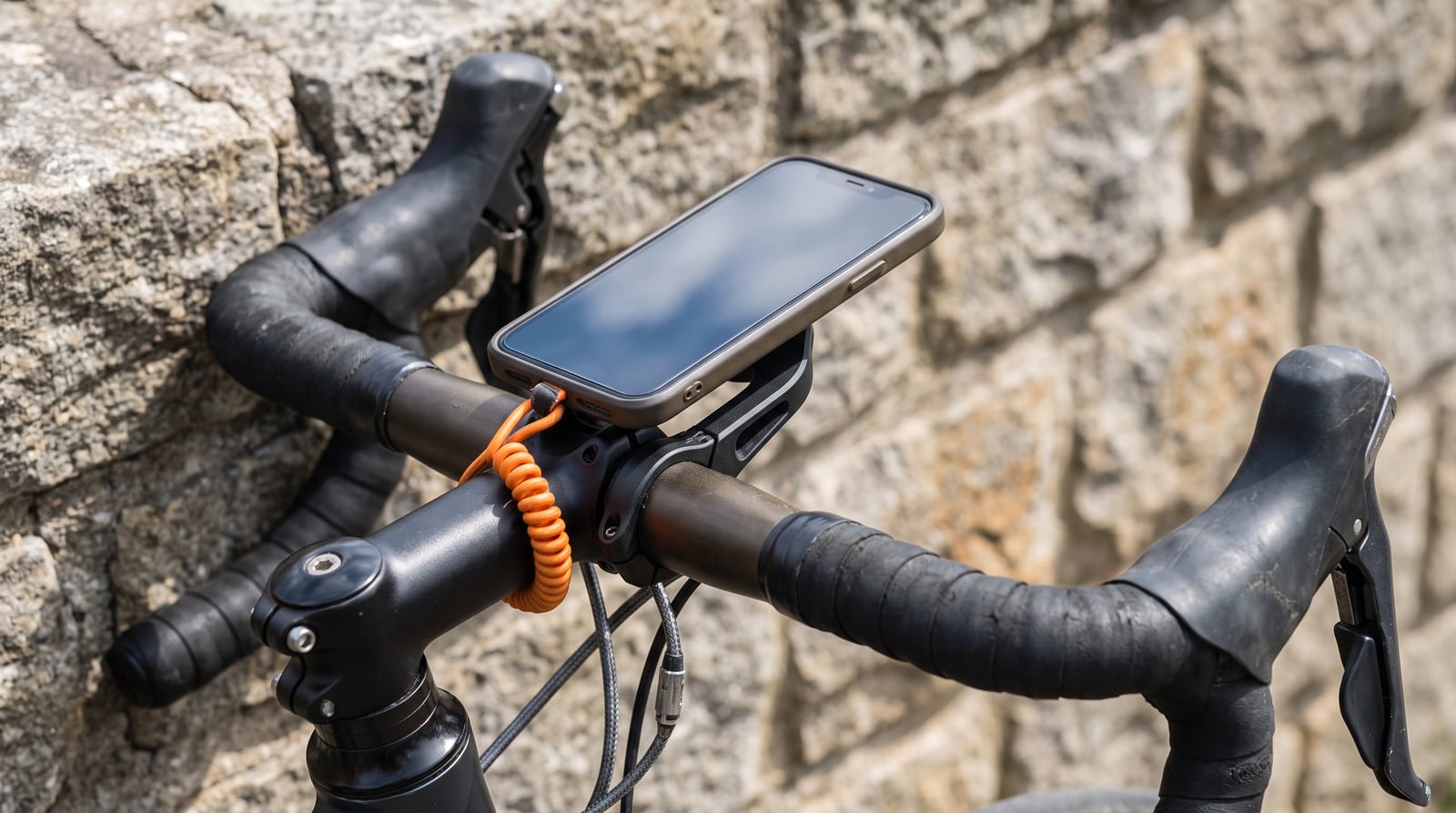 A phone on an out-front handlebar mount with a short orange safety tether looped from the case around the handlebar